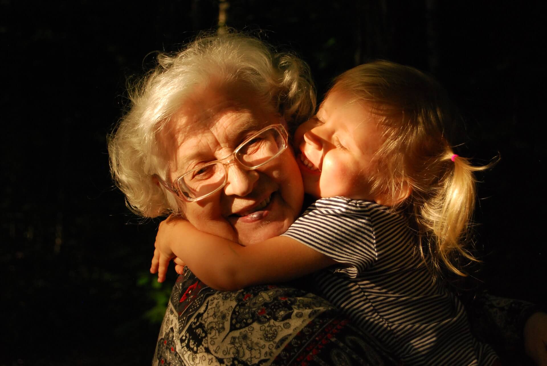 Femme âgée qui sourit avec sa petite fille qui lui fait un câlin.