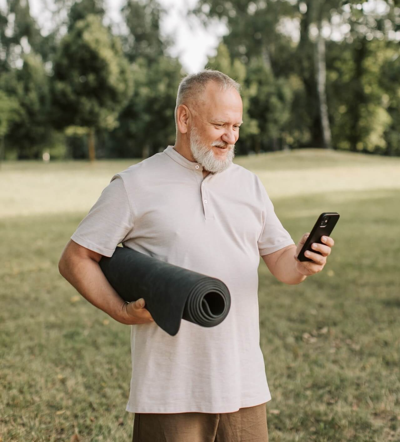 Monsieur dans un parc qui regarde son téléphone en souriant