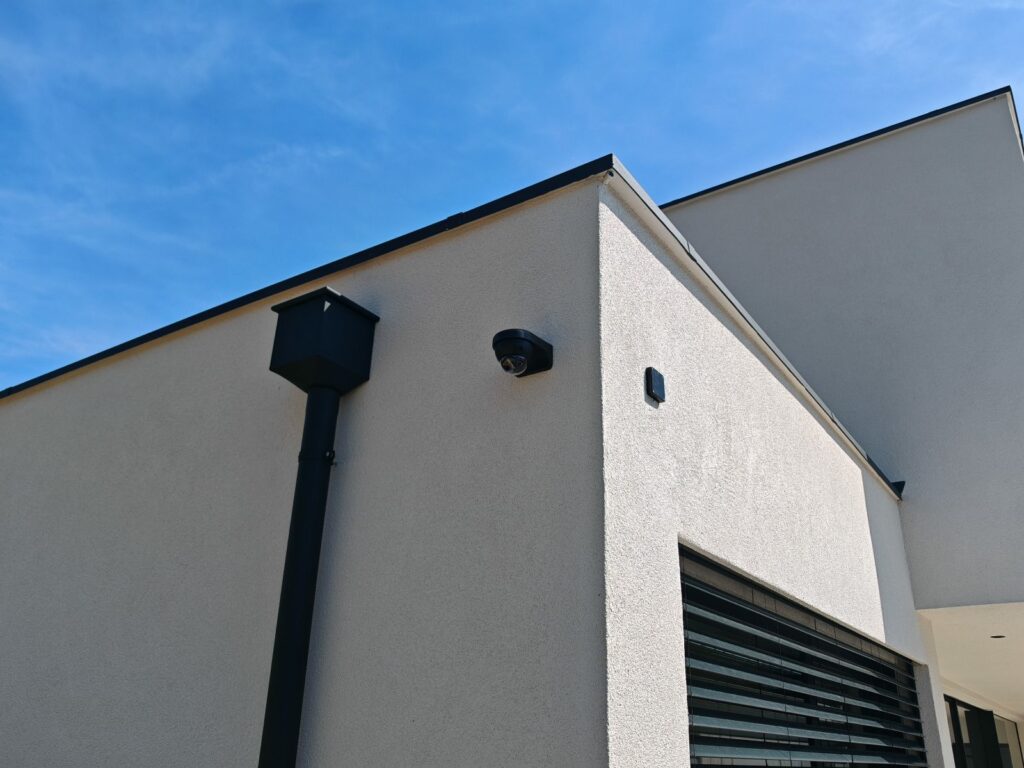 Caméra dôme noire discrètement intégrée à la façade blanche d'une villa moderne