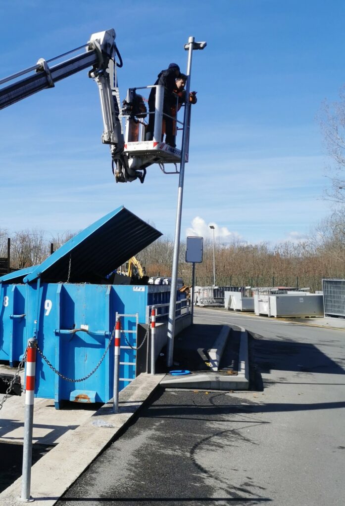 Techniciens Activ'Sécurité installant des caméras de surveillance sur un mât depuis une nacelle, au-dessus des bennes d'une déchetterie