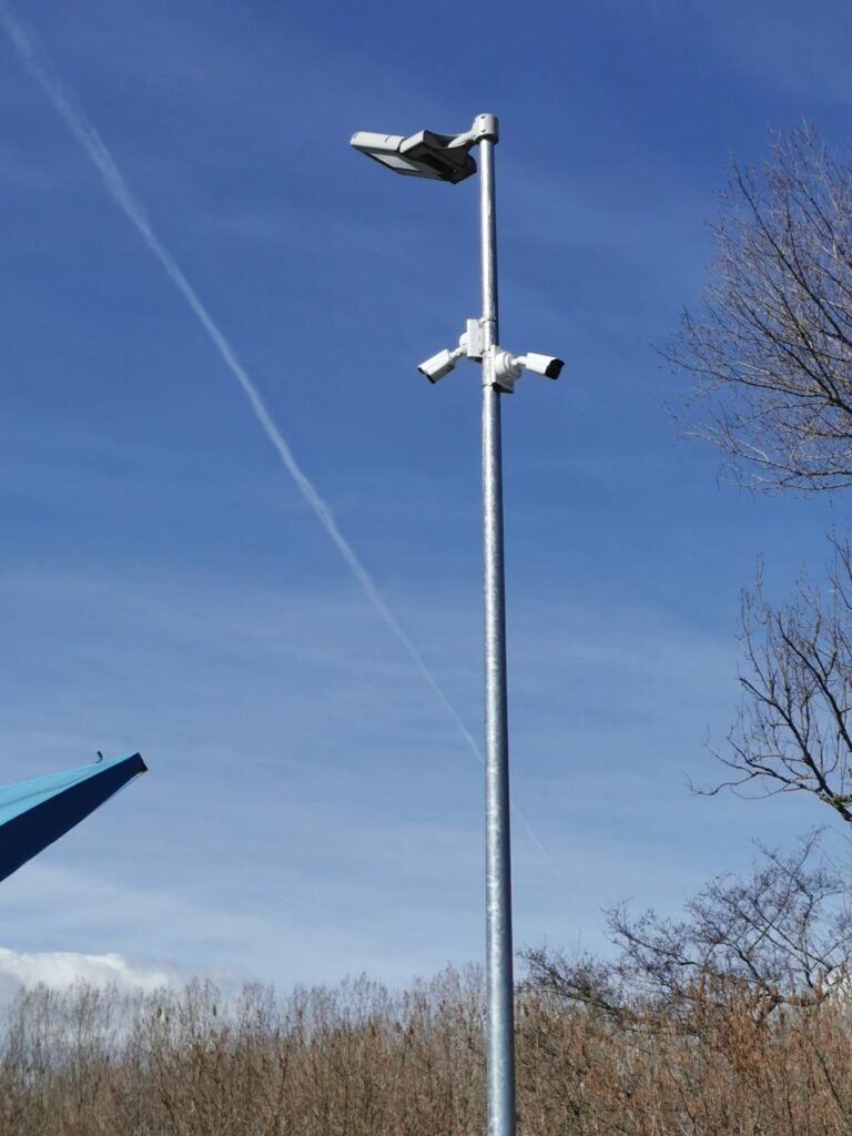 Mât galvanisé équipé de deux caméras de surveillance et d'un éclairage, surveillant les bennes d'une déchetterie