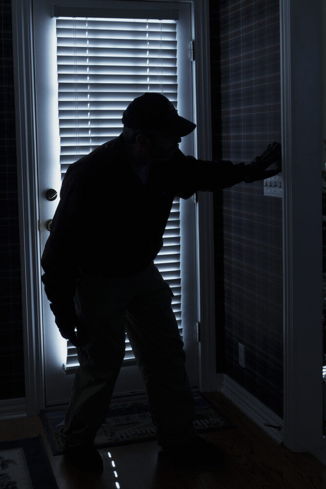 Silhouette d'un cambrioleur devant une porte-fenêtre, de nuit